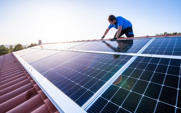 mann i blå t-skjorte monterer solcelleanlegg på tak i strålende solskinn.